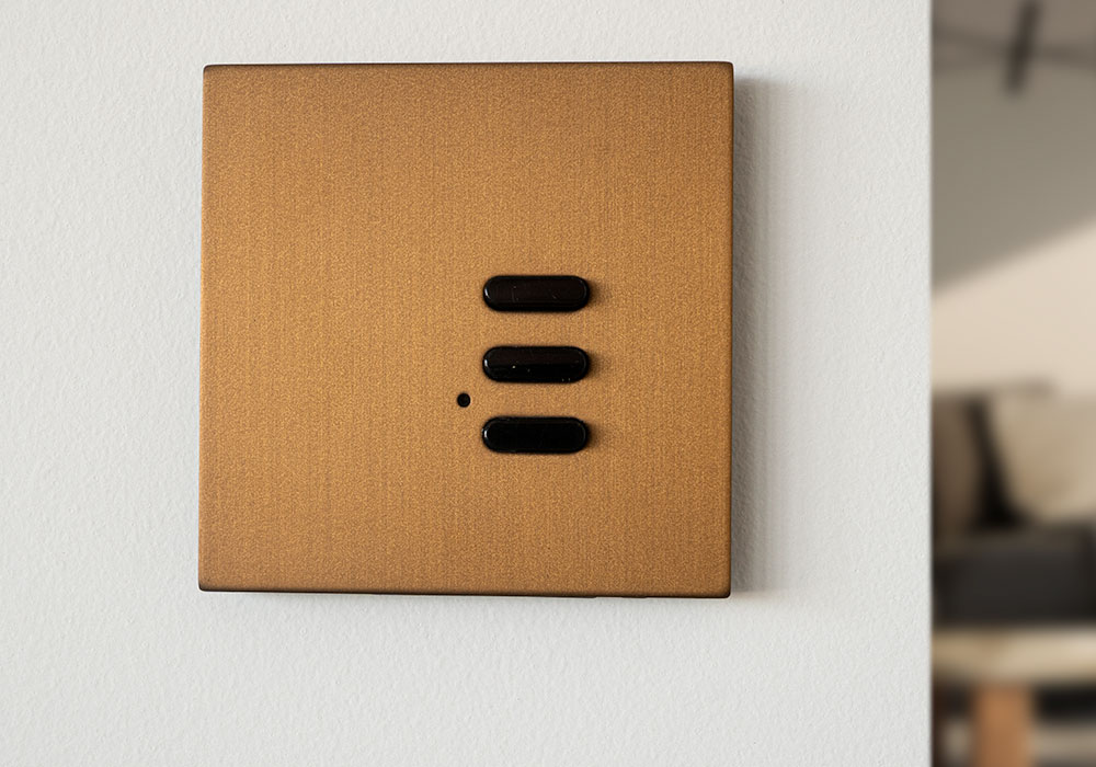 A bronze-finish Wise Scene keypad mounted on a white plaster wall
