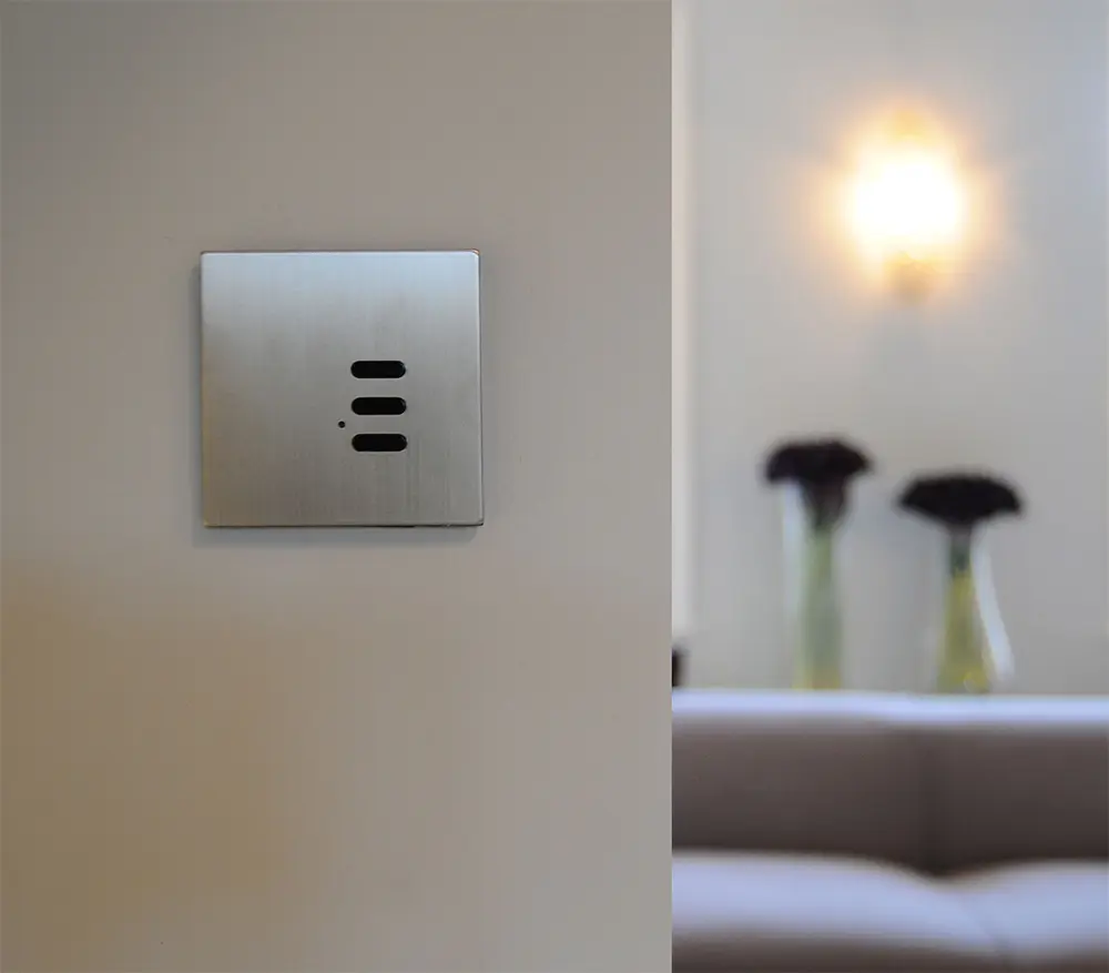 A brushed-steel Wise keypad on a cream wall with a wall sconce in the background